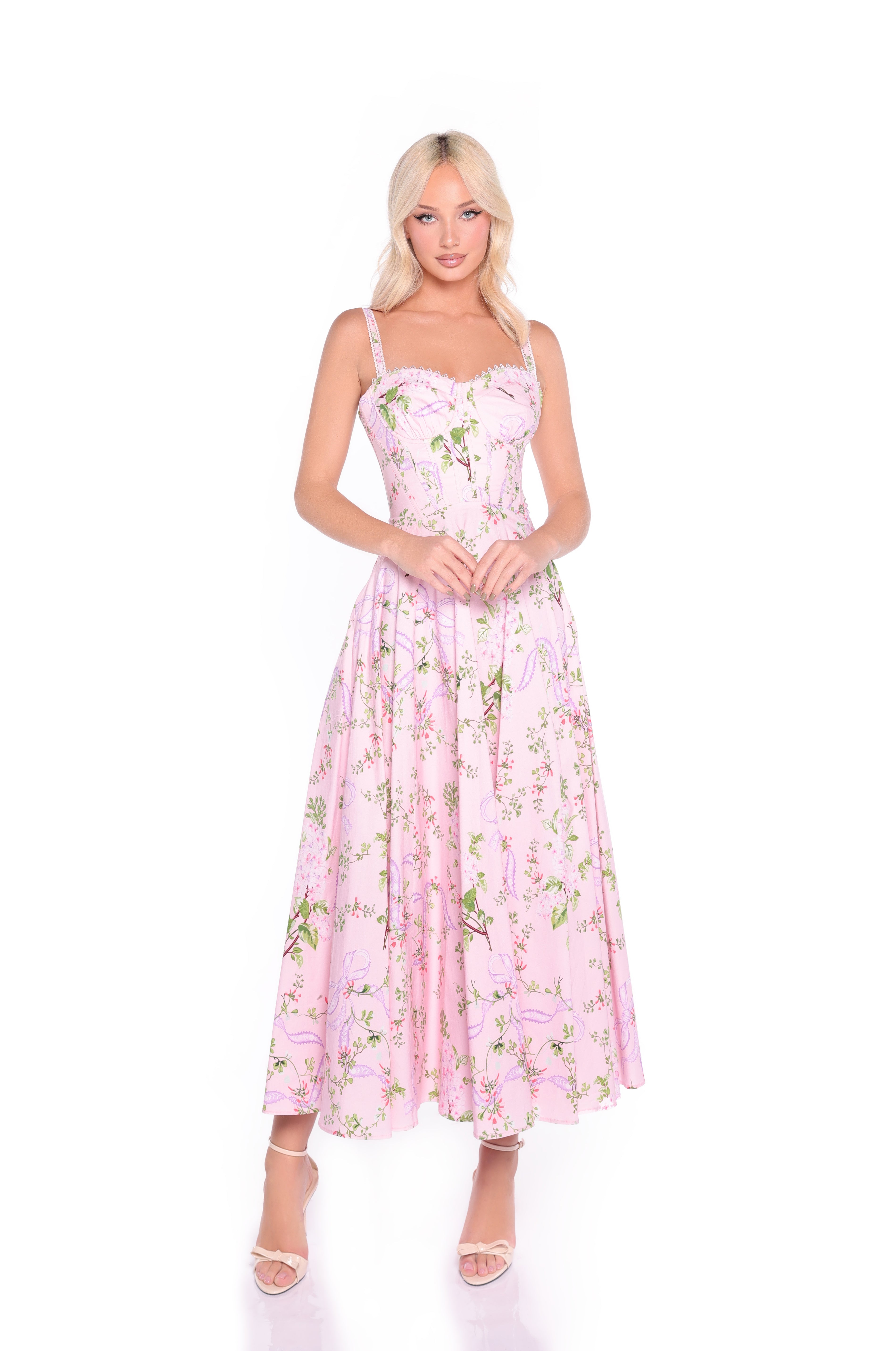 A woman in the Rosella Blush Pink Floral & Bow Print Casual Dress with spaghetti straps and open-toe heels stands against a white background—an effortlessly chic summer wedding look.